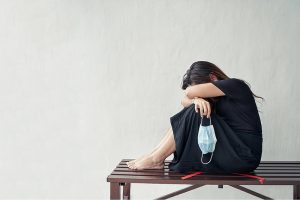 Sad and stressed woman with black outfit sitting on chair holding medical face mask.